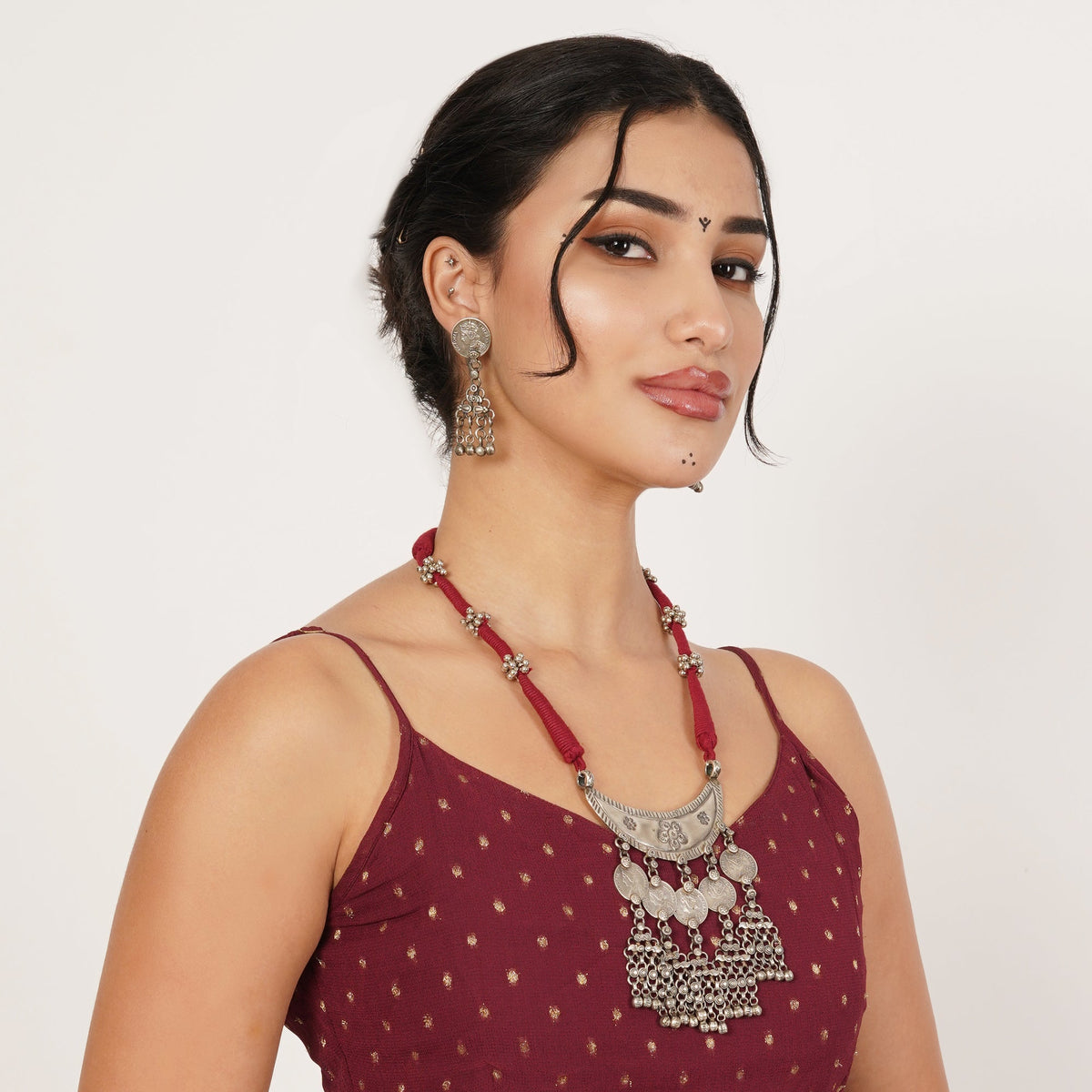 A woman wearing a deep red beaded necklace with a silver-toned ornate pendant and matching dangling earrings